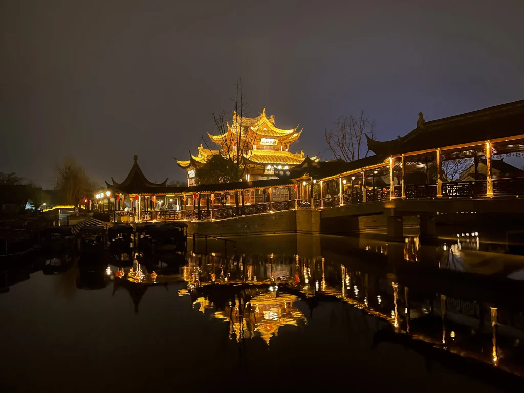 Nachts beleuchteter Baosheng Tempel mit Spiegelungen im See in der Wasserstadt Luzhi.